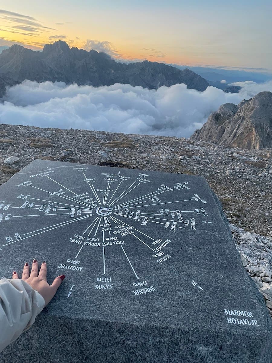 Mountain panorama above clouds with a stone orientation table marked "MARMOR HOTAVLJE