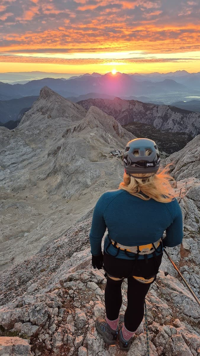 Hiker in helmet and harness viewing sunrise over rocky mountains and valleys.