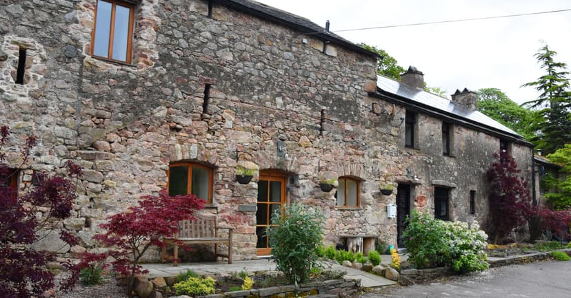 Stone cottage exterior with wooden bench, red foliage, and solar panels on the roof.