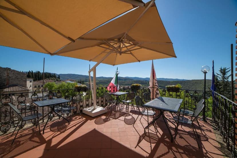 Terrace with metal tables and chairs under umbrella overlooking rolling green hills and Italian flag.