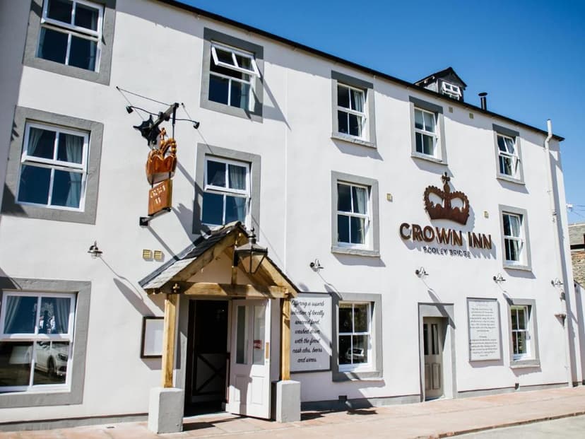The Crown Inn pub exterior in Pooley Bridge with white walls and dark window frames under blue sky.