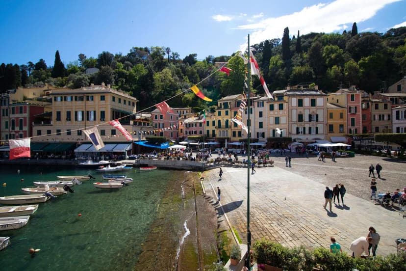 Colorful buildings line Portofino harbor with small boats and people in the sunny piazza.