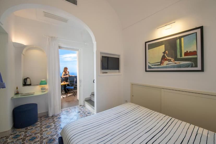Boutique hotel room with striped bedding, artwork, and balcony view of the sea.