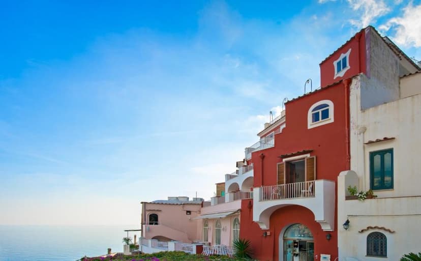 Colorful buildings of Hotel Casa Albertina overlooking the sea under a bright blue sky.