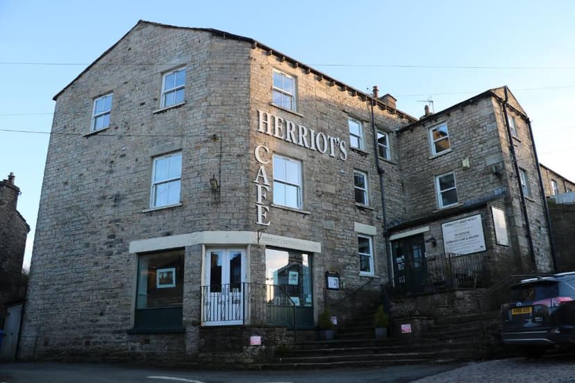 Stone building with "Herriot's Cafe" signage on a street with steps and a parked car.