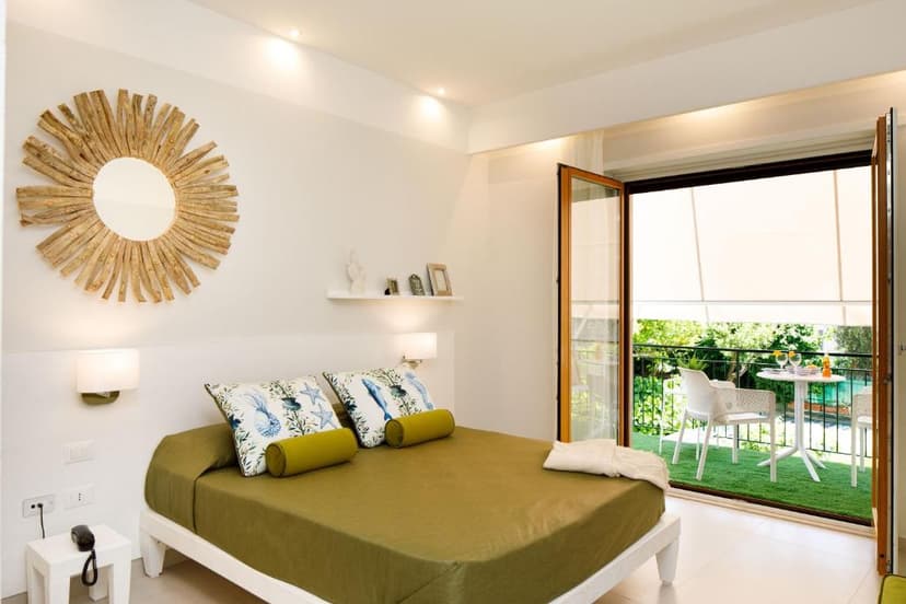 Bedroom with olive green bedding, sunburst mirror, and balcony with outdoor seating.