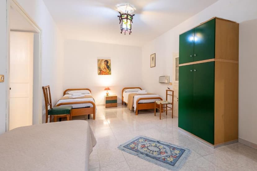 Bedroom with two single beds, white walls, tiled floor, and a large green wardrobe.
