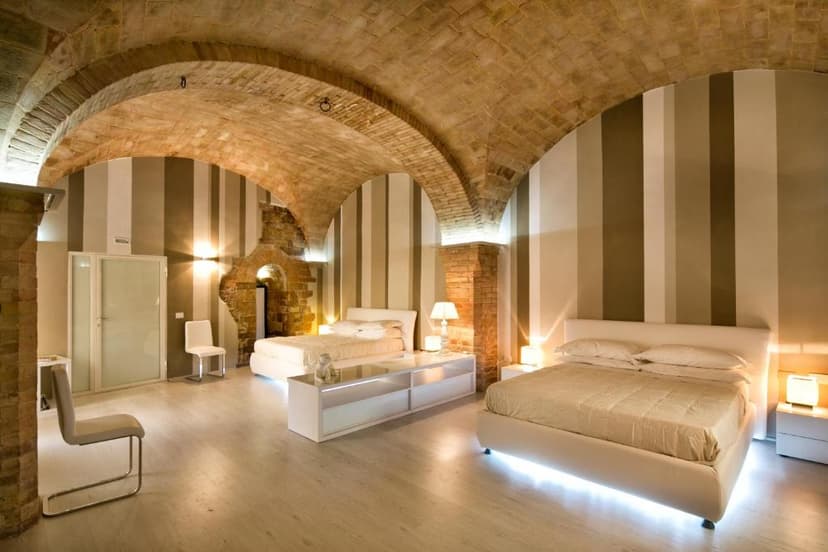 Bedroom with vaulted brick ceiling, striped walls, and modern white beds at Hotel Degli Affreschi.