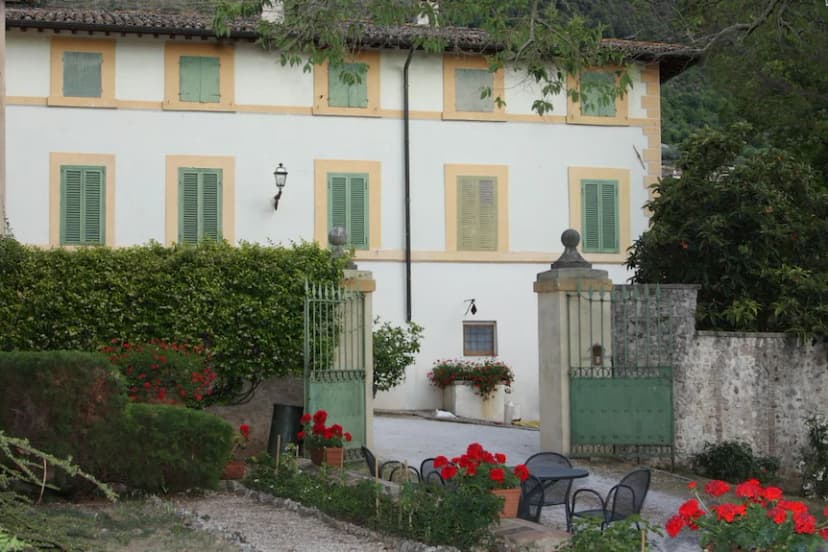 Villa del Cardinale entrance with white facade, green shutters, and red geraniums in garden.