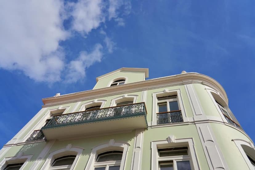 Light green hotel facade with ornate balconies against a bright blue sky with white clouds.