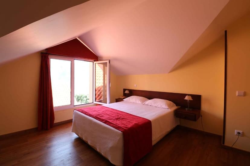 Attic hotel bedroom with double bed, wooden floor, and window view at Valley View Hotel Encumeada.