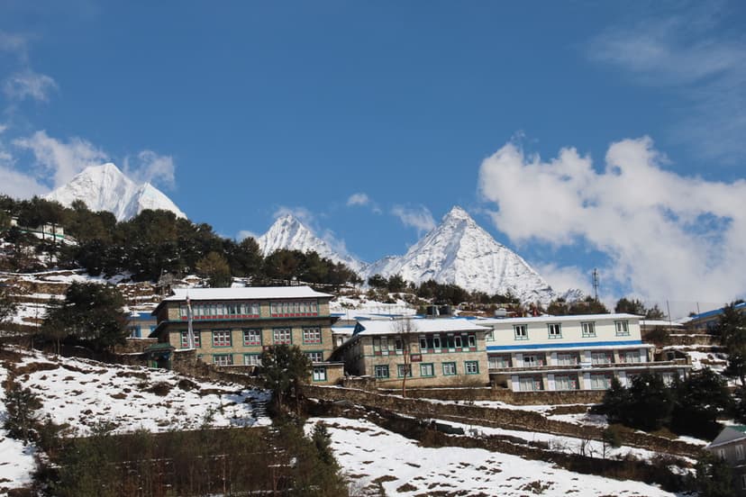 Lodge buildings in Namche Bazaar with snow-covered slopes and Himalayan peaks.