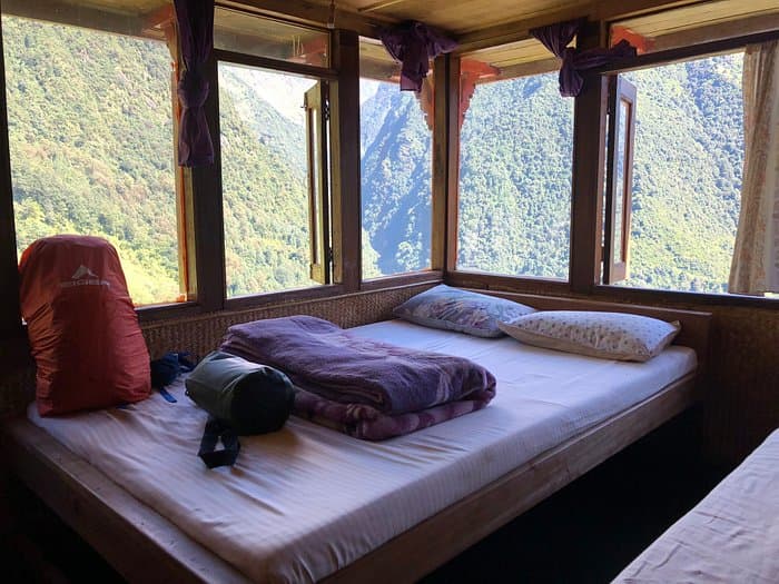 Simple lodge room with beds overlooking steep, forested mountains in Chhomrong.