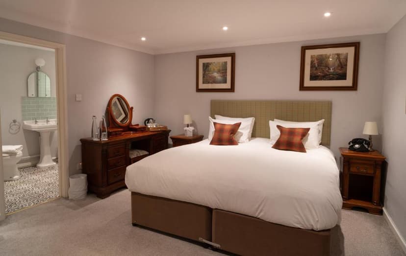 Bedroom with white bedding, wooden furniture, and view into a bathroom from the White Hart Inn.
