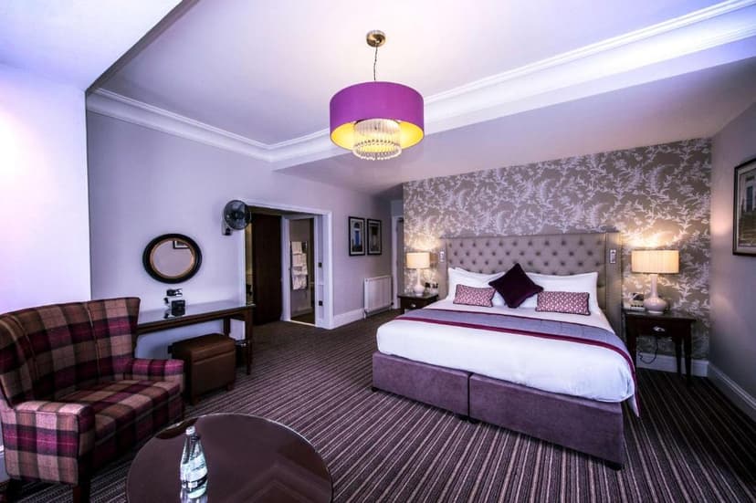 Hotel bedroom with purple chandelier, plaid armchair, and patterned wallpaper in DoubleTree by Hilton Cheltenham.