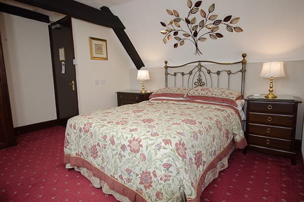 Double bedroom with floral bedding, brass bed frame, and metal tree wall art at Stow Lodge Hotel.