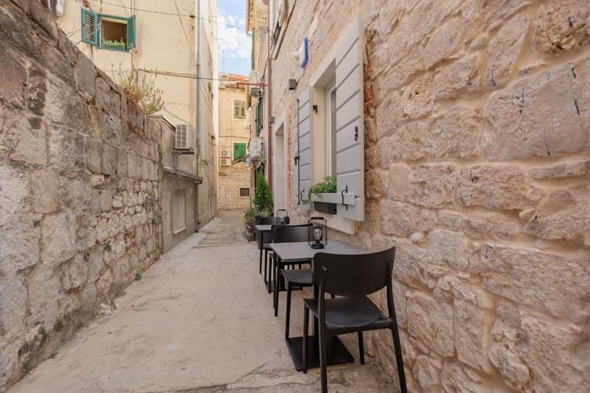 Outdoor cafe tables and chairs set up in a narrow European alley with stone walls.