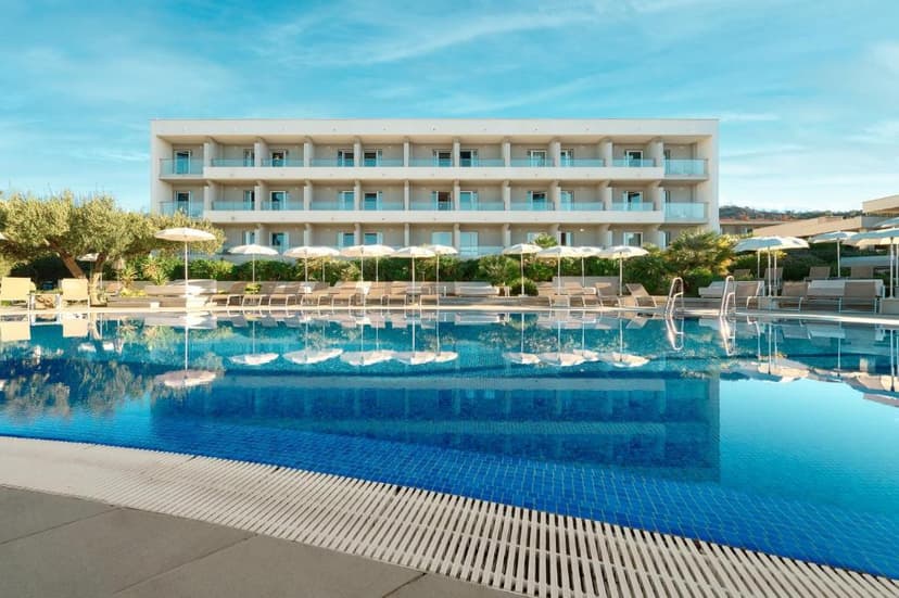 Pharos Hvar Bayhill Hotel pool with sun loungers and umbrellas reflecting in blue water.