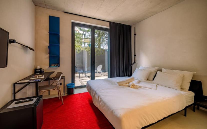 Modern hotel room with white bedding, red rug, desk, and patio access.