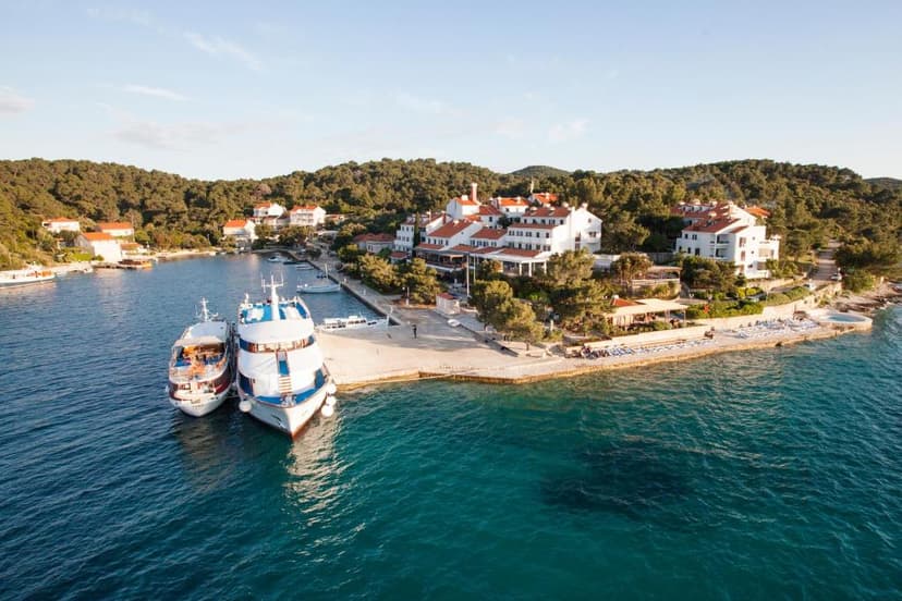 Two white passenger boats docked in a bay near white buildings on Mljet island.