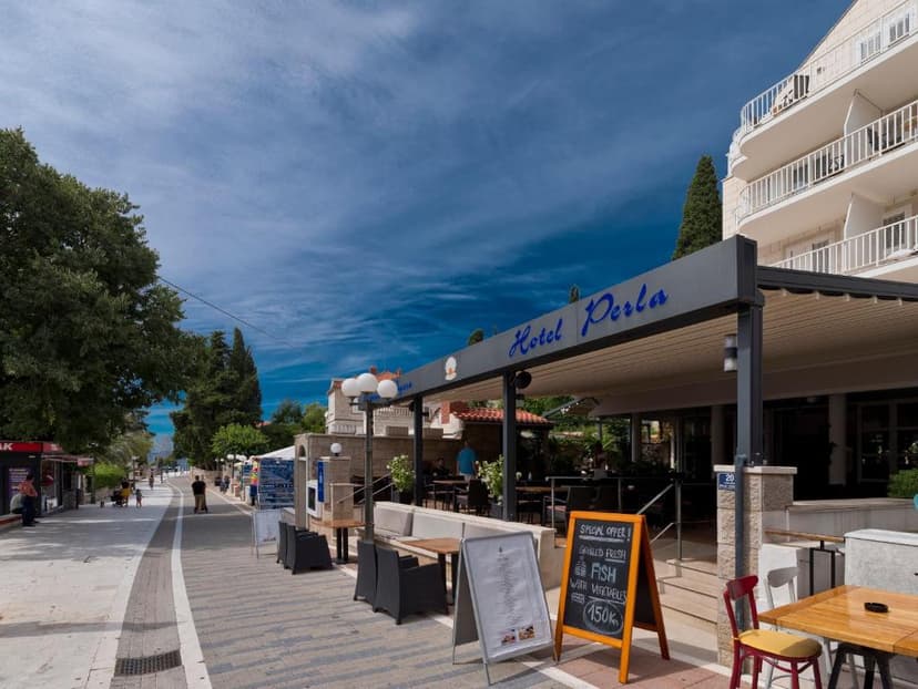 Hotel Perla outdoor dining area next to a pedestrian street under a bright blue sky.