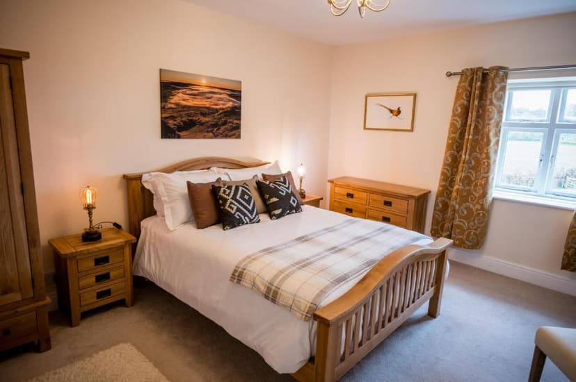 Bedroom with wooden bed frame, white linens, and window view of green fields, Abbey Farmhouse.