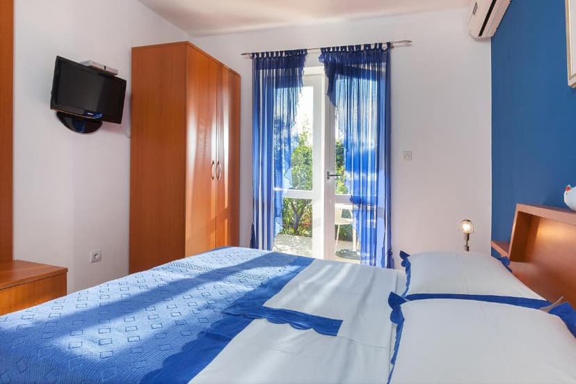 Bedroom with blue bedding, wooden wardrobe, and balcony door with sheer blue curtains