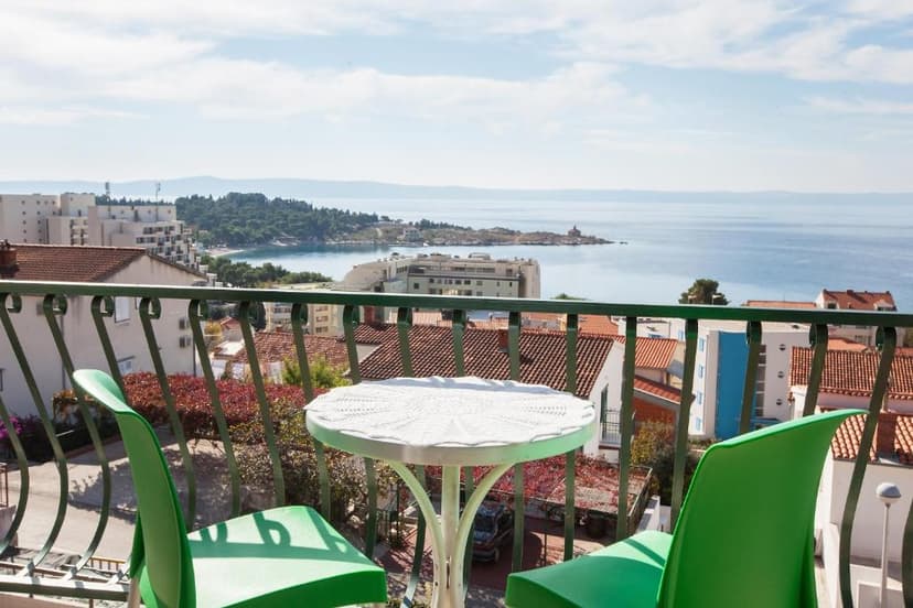 Balcony with green chairs and table overlooking coastal town and blue sea.