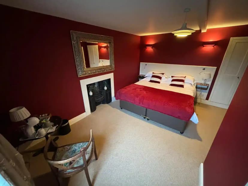 Bedroom with deep red walls, beige carpet, and a bed with red bedding in The Samson Inn.