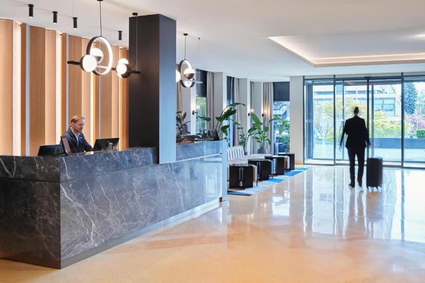 Hotel reception with marble desk, modern lighting, and guest departing through glass doors.