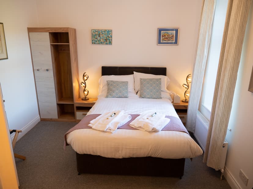 Double bed with white linens, patterned pillows, and folded towels in a hotel room at Vallum Lodge Hotel.