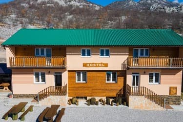 Two-story hostel building with a green roof and wooden balconies set against rocky mountains.