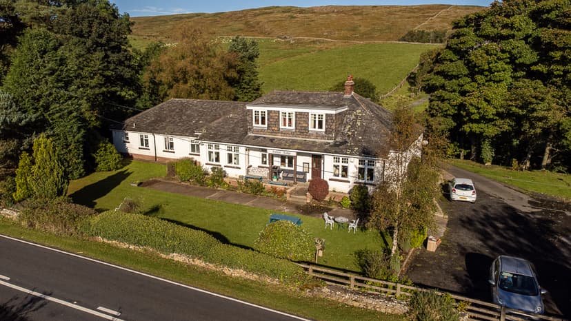 Vallum Lodge hotel building with white walls and dark roof, set against green rolling hills.