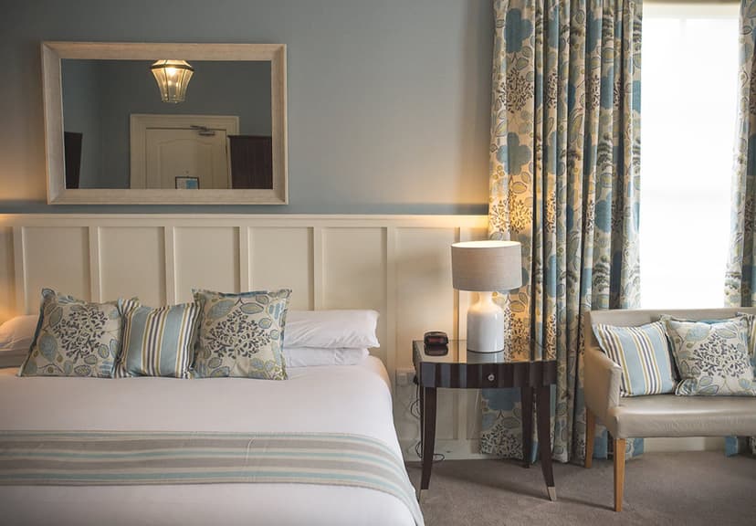 Bedroom interior with white bedding, patterned pillows, and blue floral curtains in George Hotel.