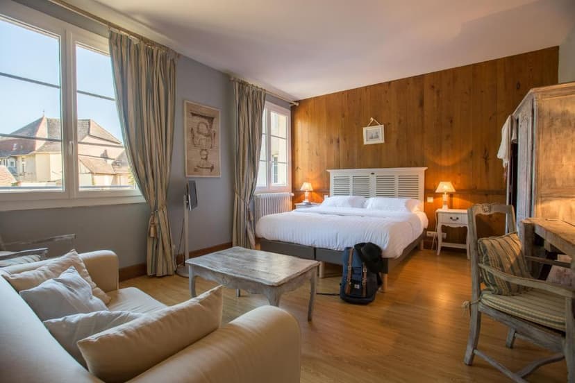 Hotel Logis Hôtel Le Beaulieu bedroom with white bedding, wood paneling, and view of rooftops.