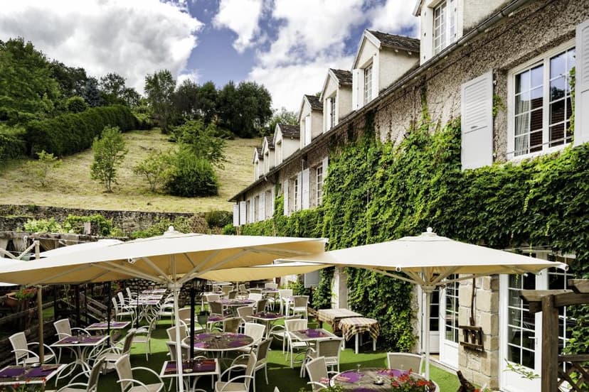Outdoor dining terrace at Logis Hôtel Le Beaulieu against ivy-covered stone building.