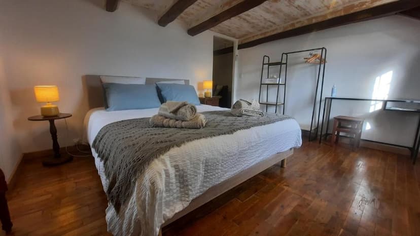 Bedroom with double bed, wood floor, exposed beams, and modern black shelving unit.