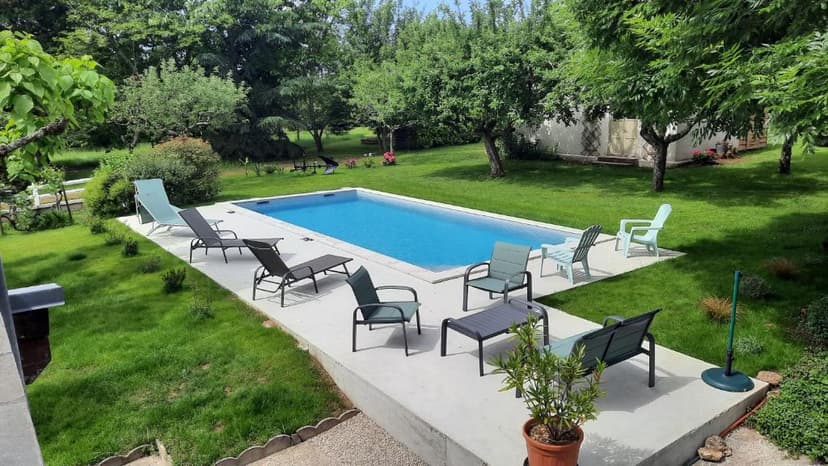 Swimming pool surrounded by green lawn, lounge chairs, and trees at L'Ostal de Gagnac.