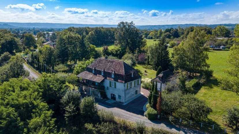 L'Ostal de Gagnac building surrounded by lush green trees and fields under a blue sky.