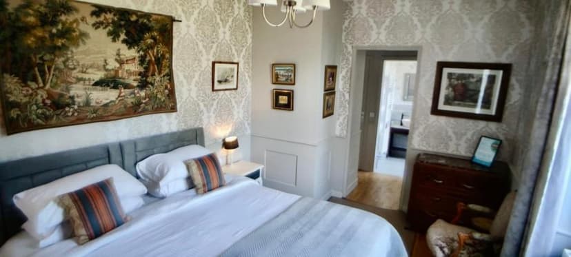 Bedroom with large tapestry, white bedding, and patterned wallpaper leading to bathroom