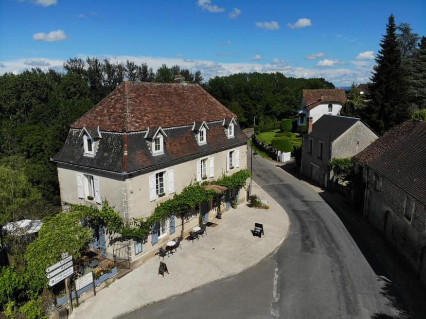 Auberge with vine-covered facade and outdoor tables on a curved road in a village setting.