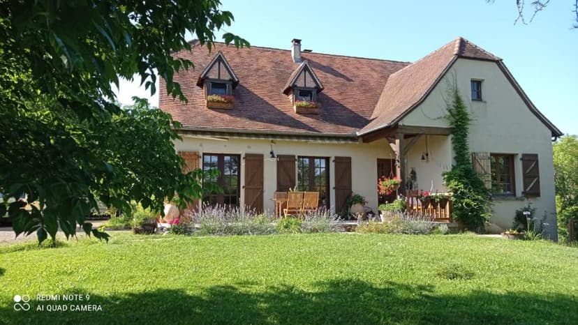 Traditional house with terracotta roof and wooden shutters overlooking a sunny green lawn in Meyronne.
