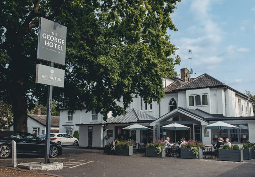 The George Hotel sign next to white building with outdoor dining area and parked cars.