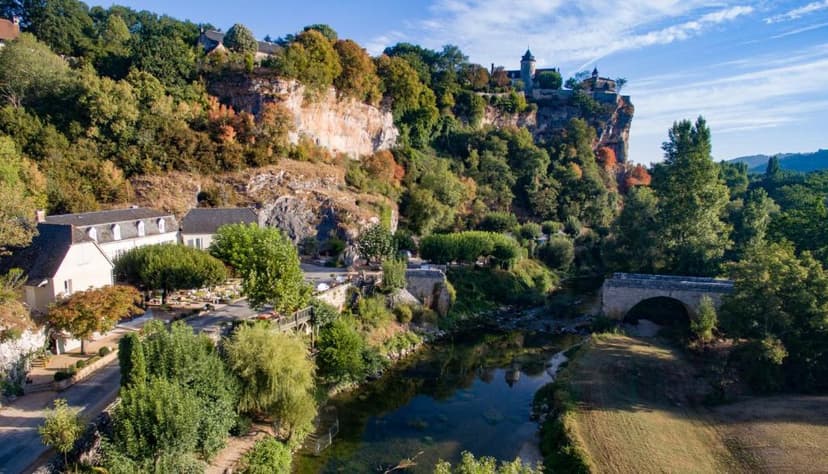 Village with buildings nestled against a cliff, stone bridge over river, Le Pont de L'Ouysse.