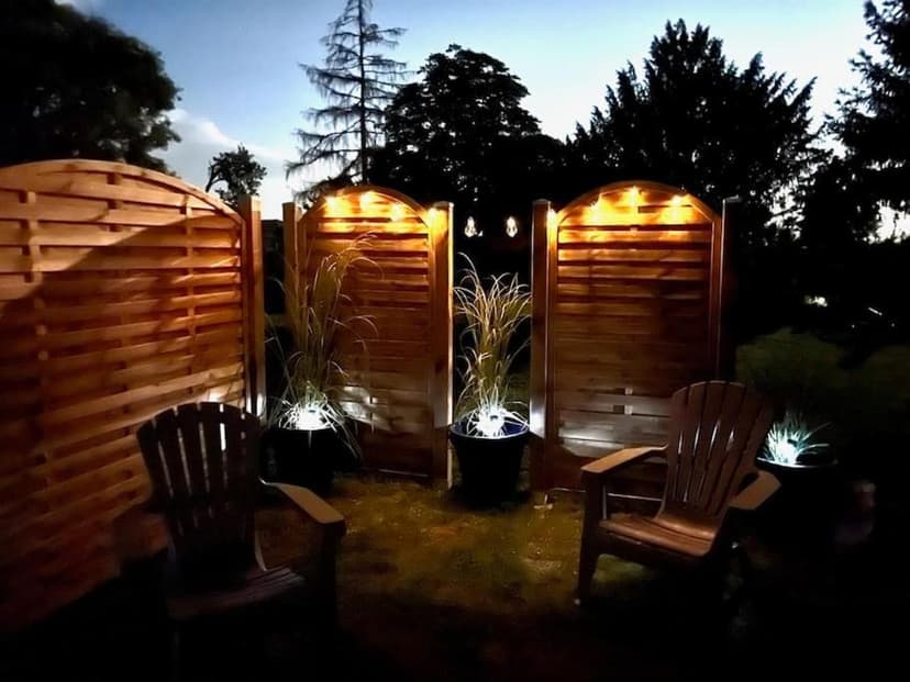 Wooden Adirondack chairs on grass patio with illuminated wooden privacy screens at night