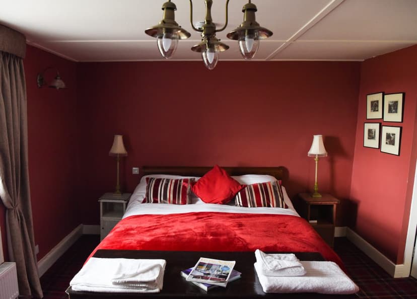 Bedroom with red walls, brass chandelier, and double bed with red bedding at Robin Hood Inn.