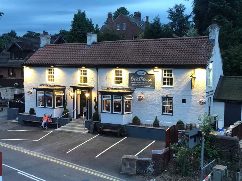 White pub named "The Boathouse" illuminated at dusk with two people sitting outside.