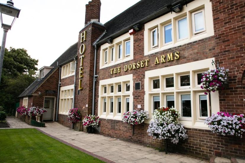 The Dorset Arms Hotel exterior with brick facade, white-framed windows, and hanging flower baskets.