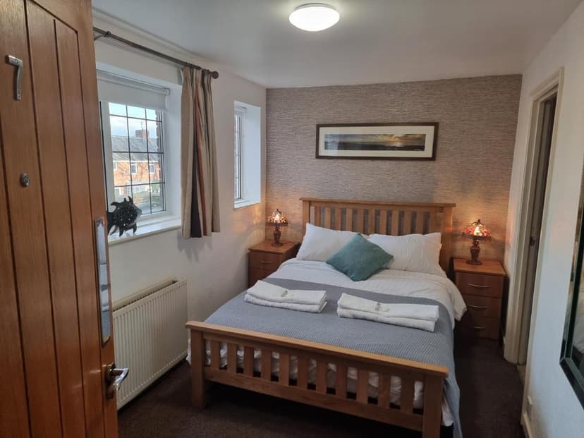 Double bedroom with wooden bed frame, textured wallpaper, and window view of buildings, Dorset Arms Hotel.