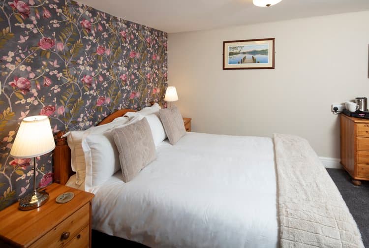 Bedroom with floral wallpaper, white bedding, and wooden nightstands with lamps.